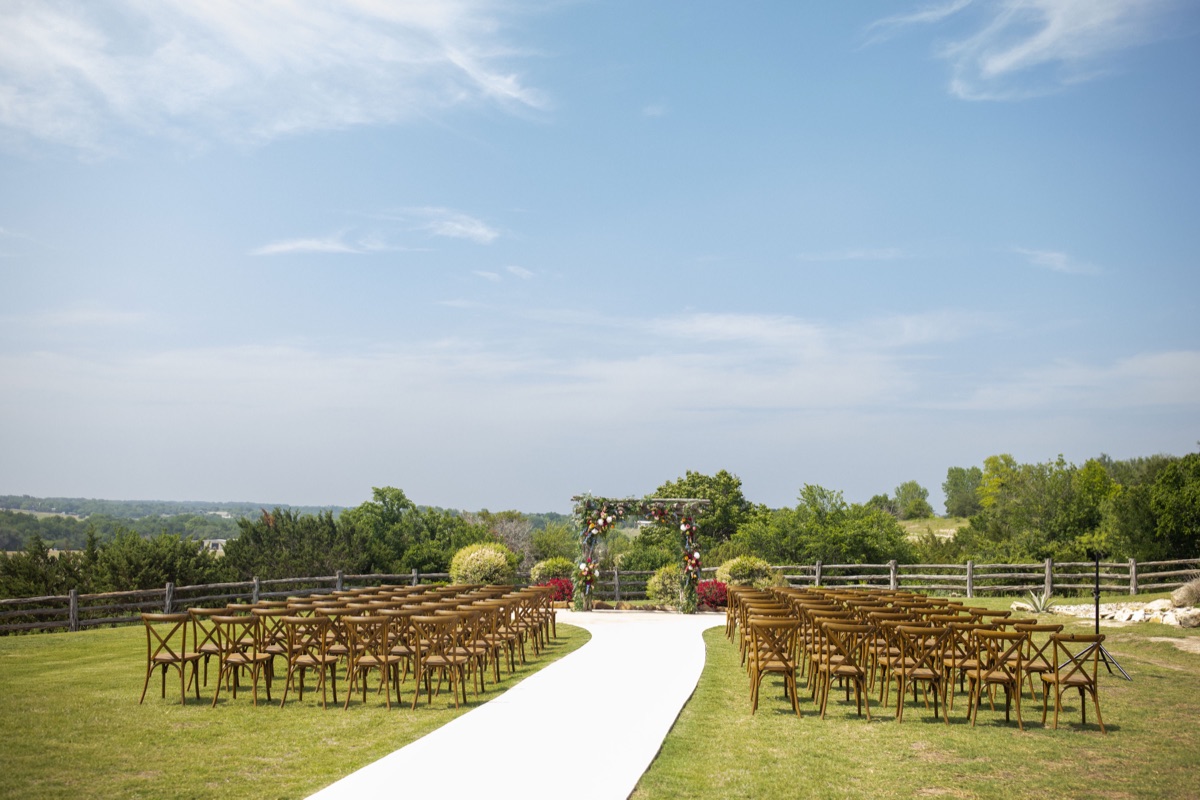 The hilltop ceremony lawn at Diamond H3 Ranch, a white aisle leading to a floral arbor with sweeping hill-country views