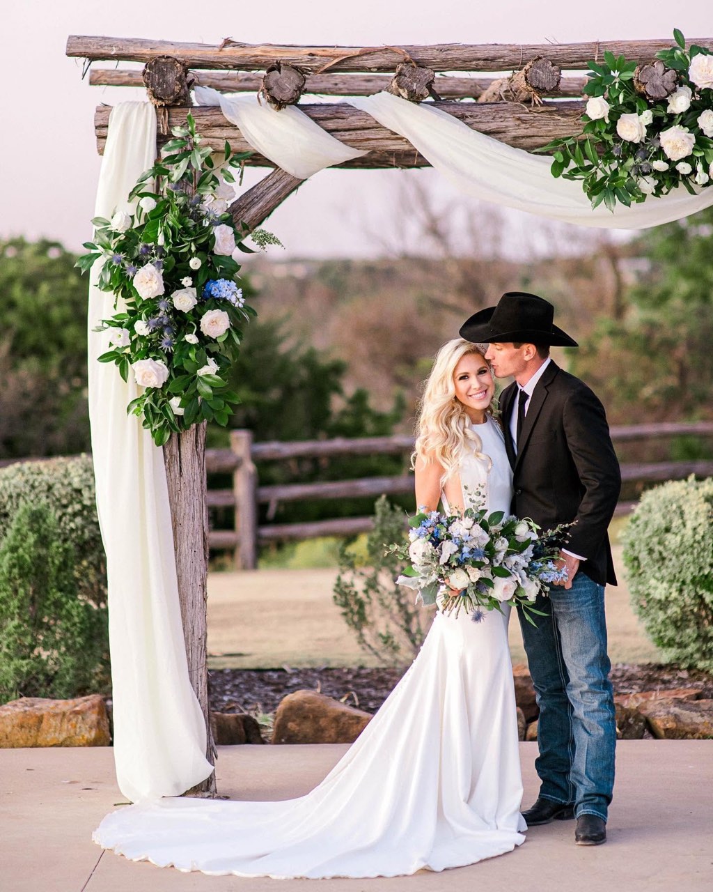 A bride and groom under the floral wooden arbor at the Diamond H3 Ranch hilltop ceremony
